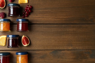 Jars of different jams and fresh ingredients on wooden table, flat lay. Space for text