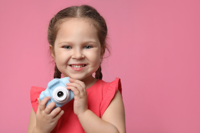 Little photographer with toy camera on pink background