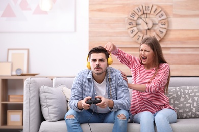 Photo of Young woman trying to draw attention of her man playing video games at home