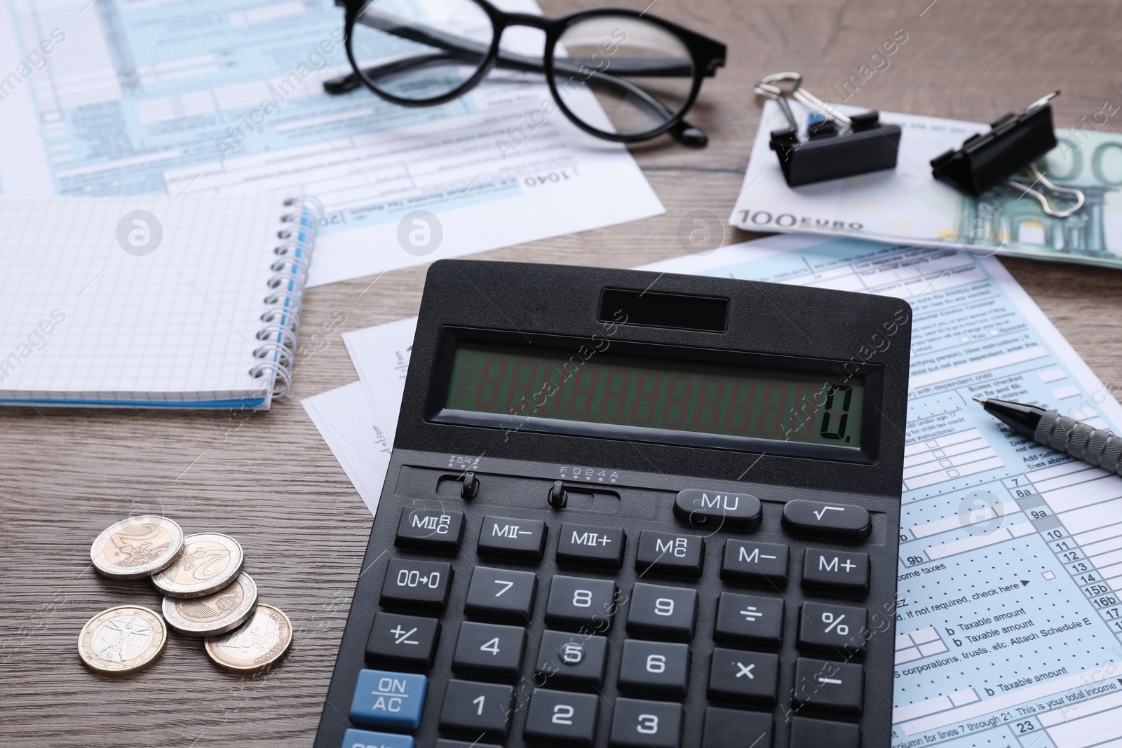 Photo of Tax accounting. Calculator, documents, stationery and glasses on wooden table, closeup