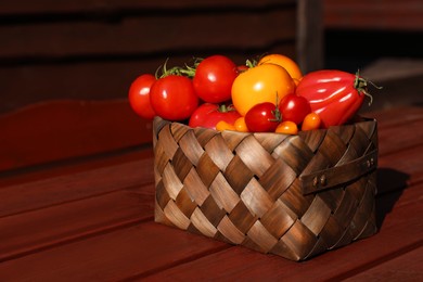 Basket with fresh tomatoes on wooden table outdoors. Space for text