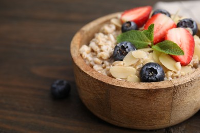 Photo of Tasty oatmeal with strawberries, blueberries and almond flakes in bowl on wooden table, closeup. Space for text