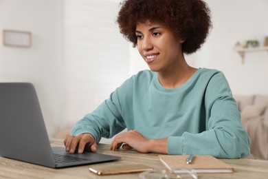 Young woman using laptop at wooden desk in room