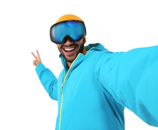 Photo of Smiling young man in ski goggles taking selfie and showing peace sign on white background