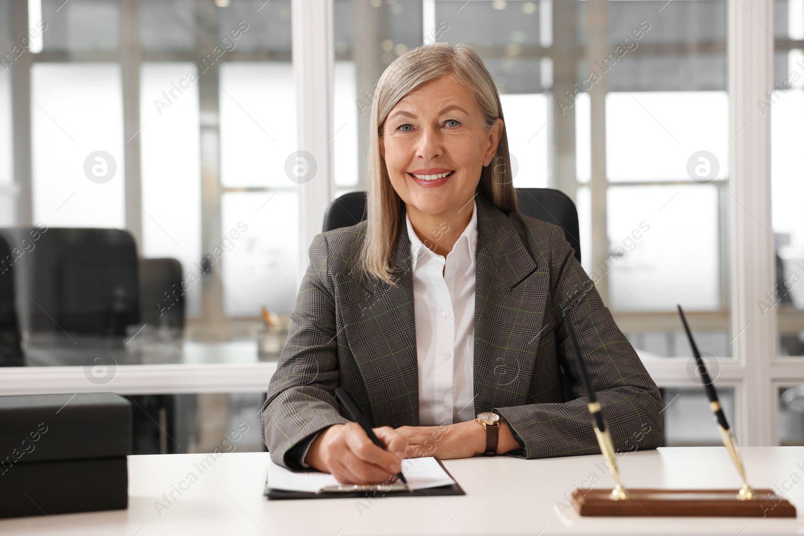 Photo of Smiling woman working at table in office. Lawyer, businesswoman, accountant or manager