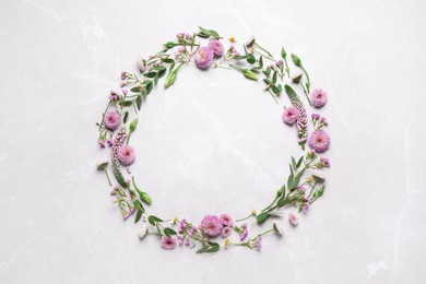 Photo of Wreath made of beautiful flowers and green leaves on light grey marble background, flat lay. Space for text