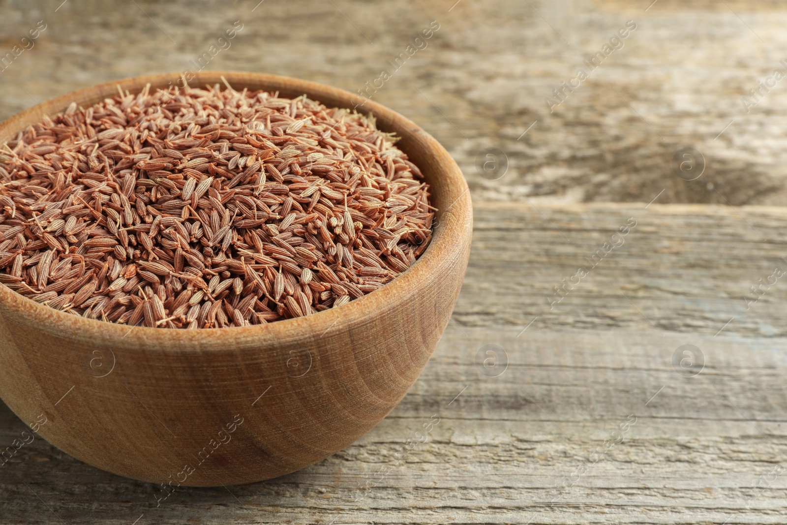 Photo of Bowl of caraway seeds on wooden table, closeup. Space for text