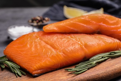 Wooden board with salmon fillet on grey table, closeup