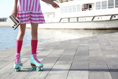 Photo of Young woman with vintage roller skates and radio on embankment, closeup view