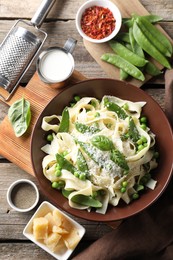 Photo of Delicious pasta with green peas and ingredients on wooden table, flat lay