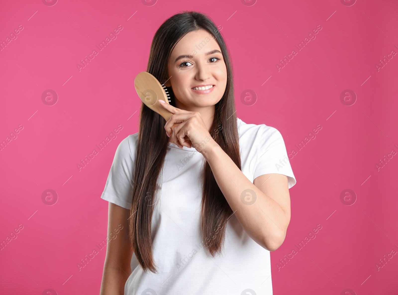 Photo of Beautiful smiling young woman with hair brush on color background