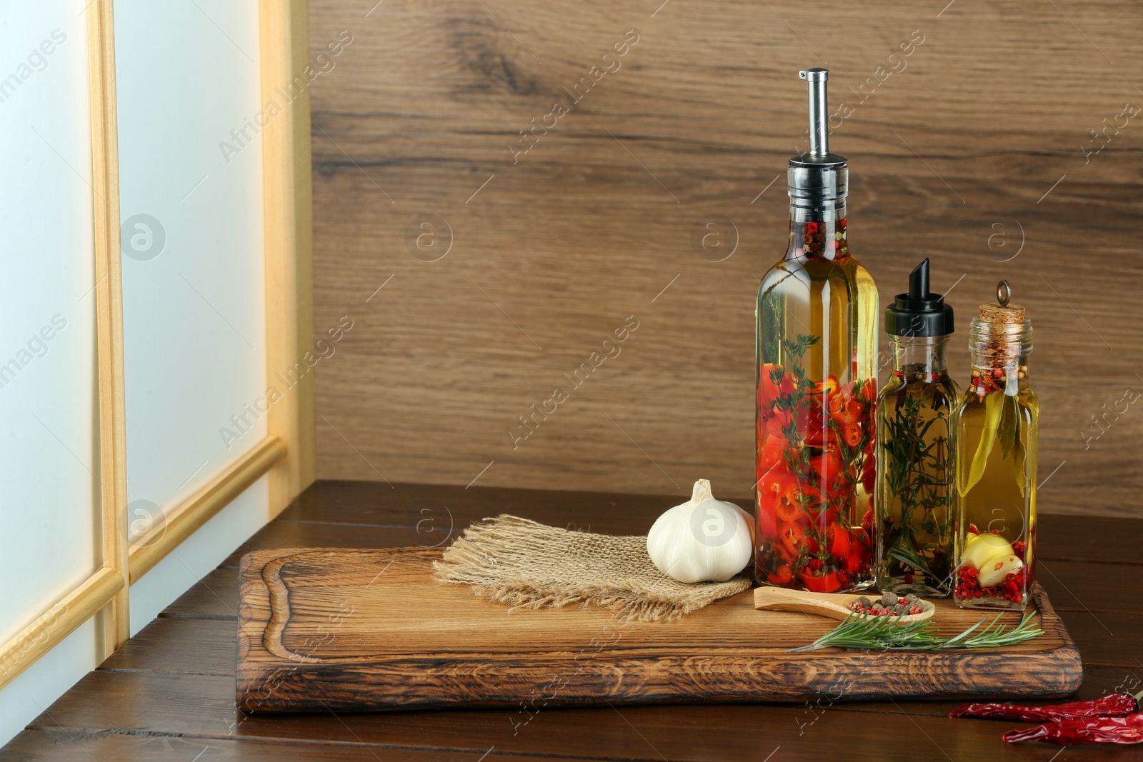 Photo of Cooking oil with different spices and herbs in bottles on wooden table. Space for text