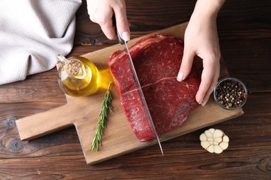 Photo of Woman cutting fresh raw beef steak at wooden table, top view