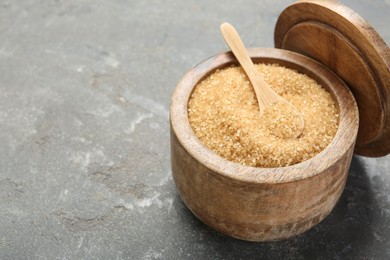 Brown sugar in bowl and spoon on grey textured table, closeup. Space for text