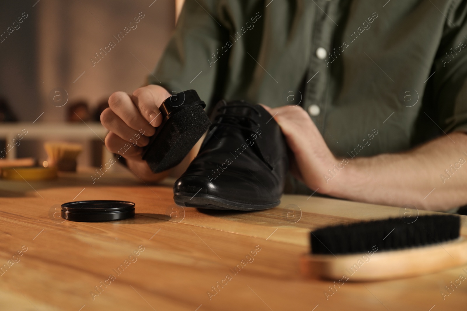 Photo of Man taking professional care of black leather shoe in workshop, closeup