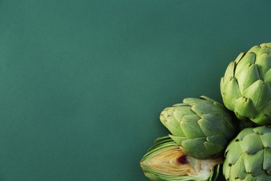 Photo of Cut and whole fresh raw artichokes on green background, flat lay. Space for text