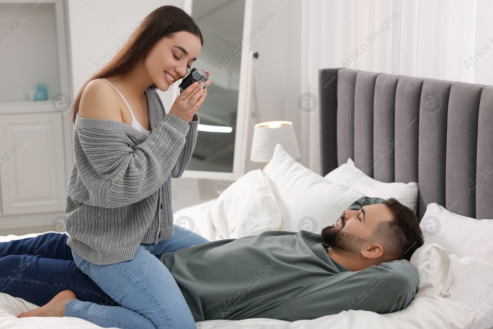 Photo of Happy young couple spending time in bedroom. Smiling woman taking photo of her boyfriend