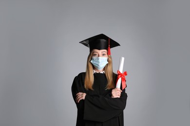 Student in protective mask with diploma on grey background