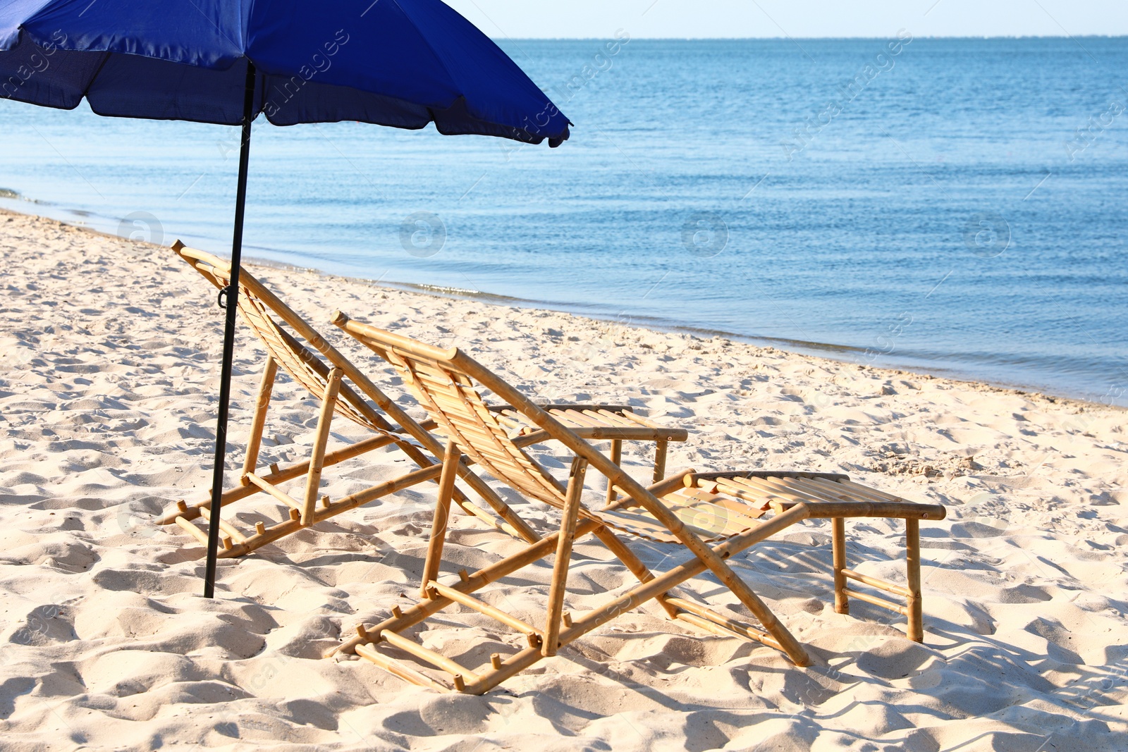 Photo of Empty wooden sunbeds and umbrella on sandy shore. Beach accessories