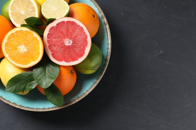 Photo of Different cut and whole citrus fruits on black table, top view. Space for text