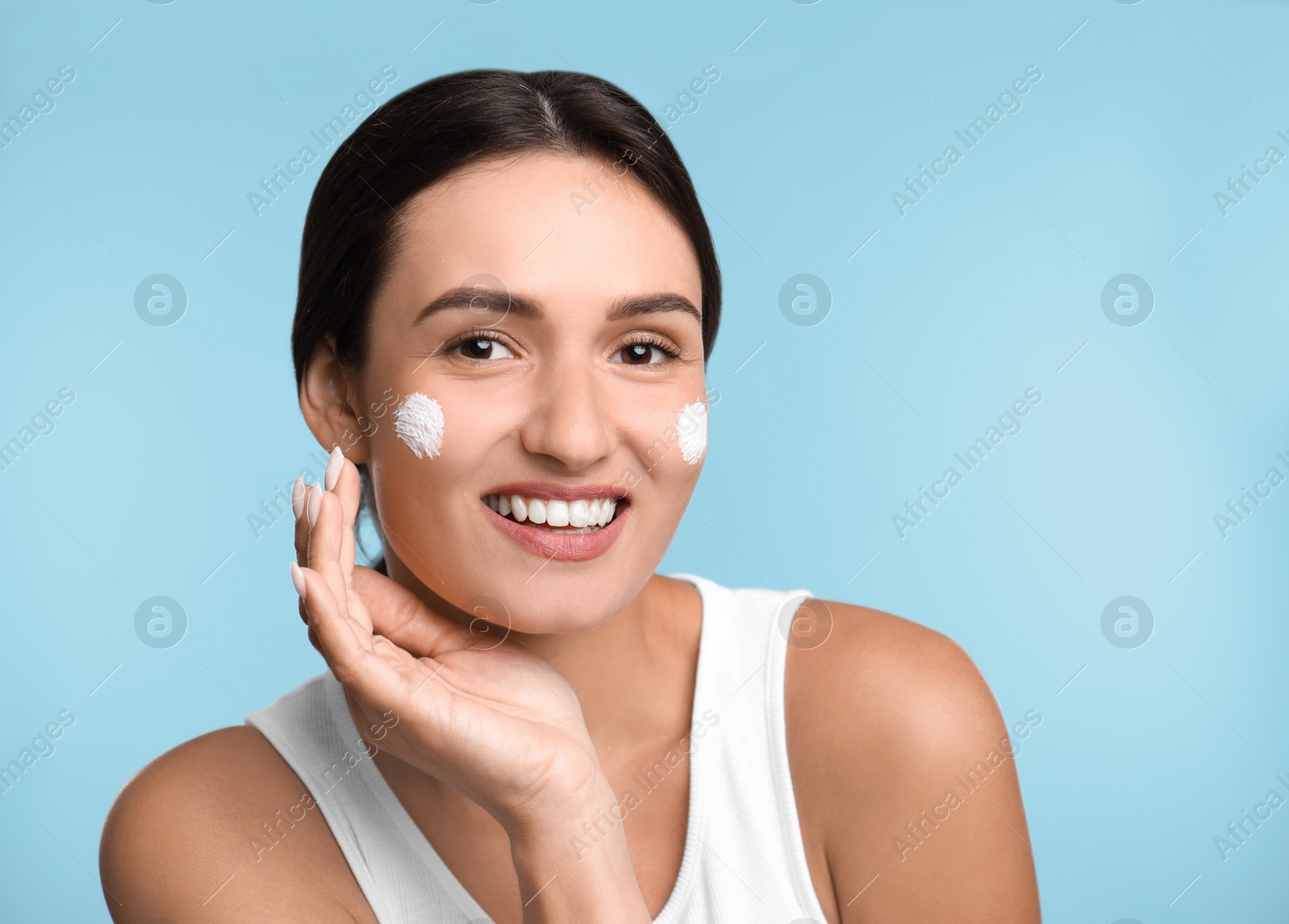 Photo of Young woman applying facial cream on light blue background