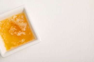 Photo of Melted butter in bowl on white wooden table, top view. Space for text