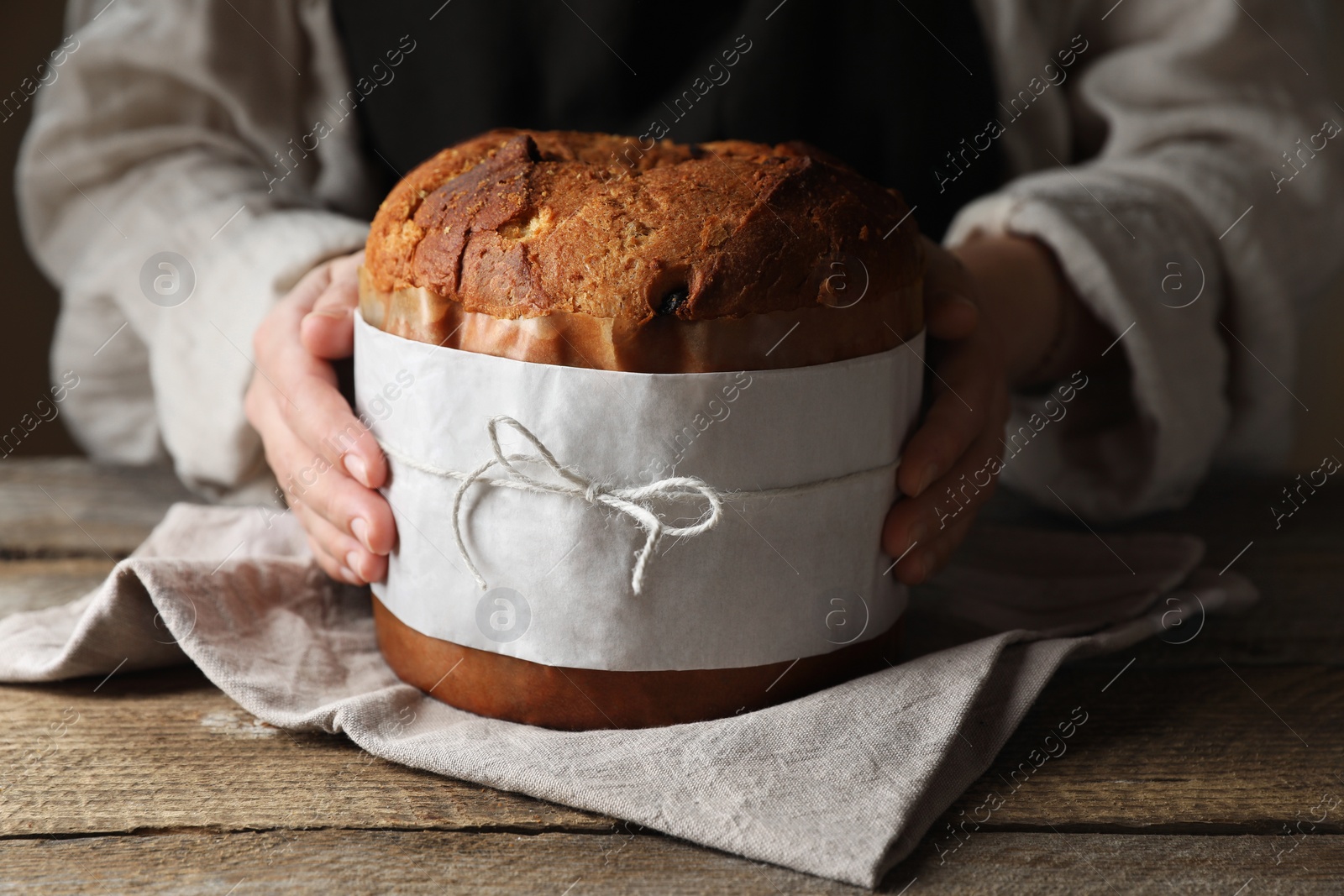 Photo of Woman holding delicious Panettone cake at wooden table, closeup. Traditional Italian pastry