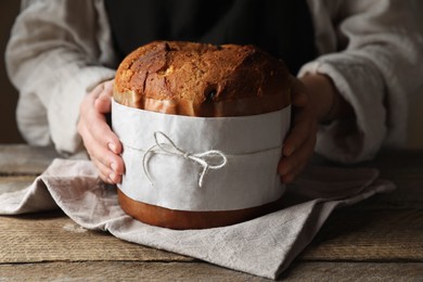 Woman holding delicious Panettone cake at wooden table, closeup. Traditional Italian pastry