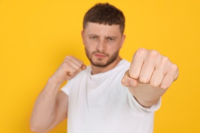 Young man ready to fight against orange background, focus on hand. Space for text