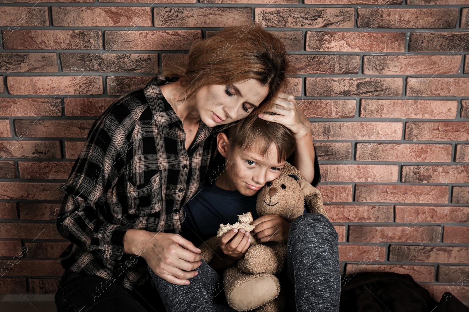 Photo of Poor woman hugging her son near brick wall