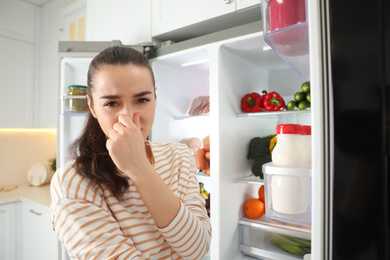 Photo of Young woman holding nose cause of bad smell in refrigerator in kitchen