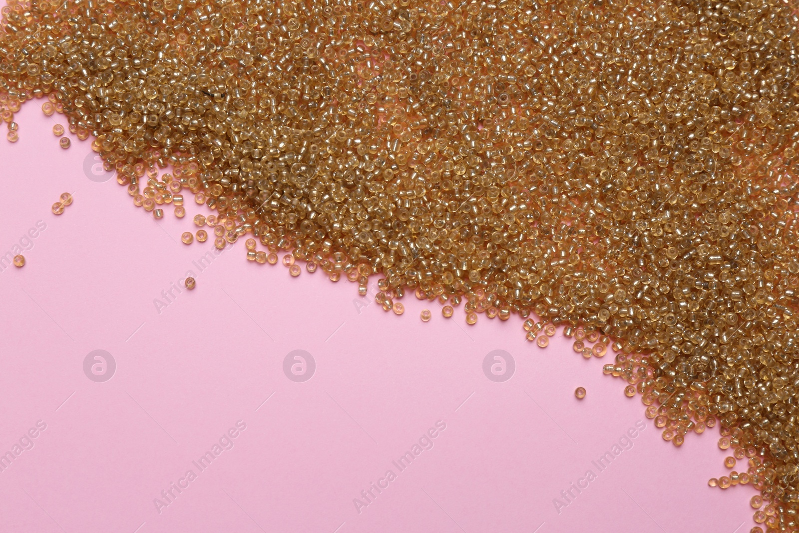 Photo of Bright golden glass beads on pink background, flat lay. Space for text