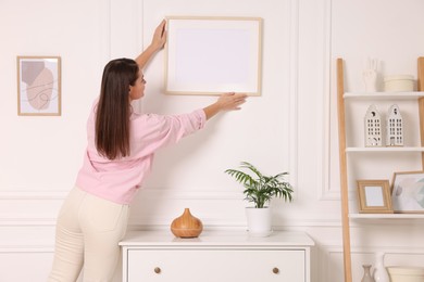 Woman hanging picture frame on white wall at home