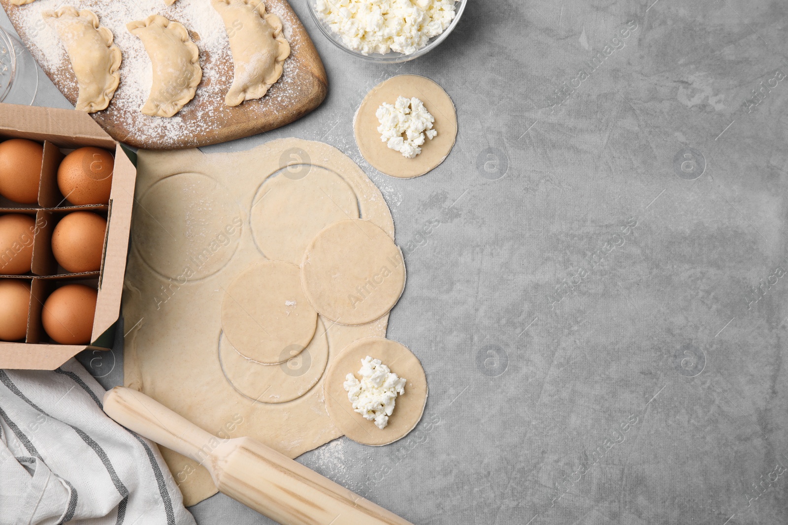 Photo of Process of making dumplings (varenyky) with cottage cheese. Raw dough and ingredients on grey table, flat lay. Space for text