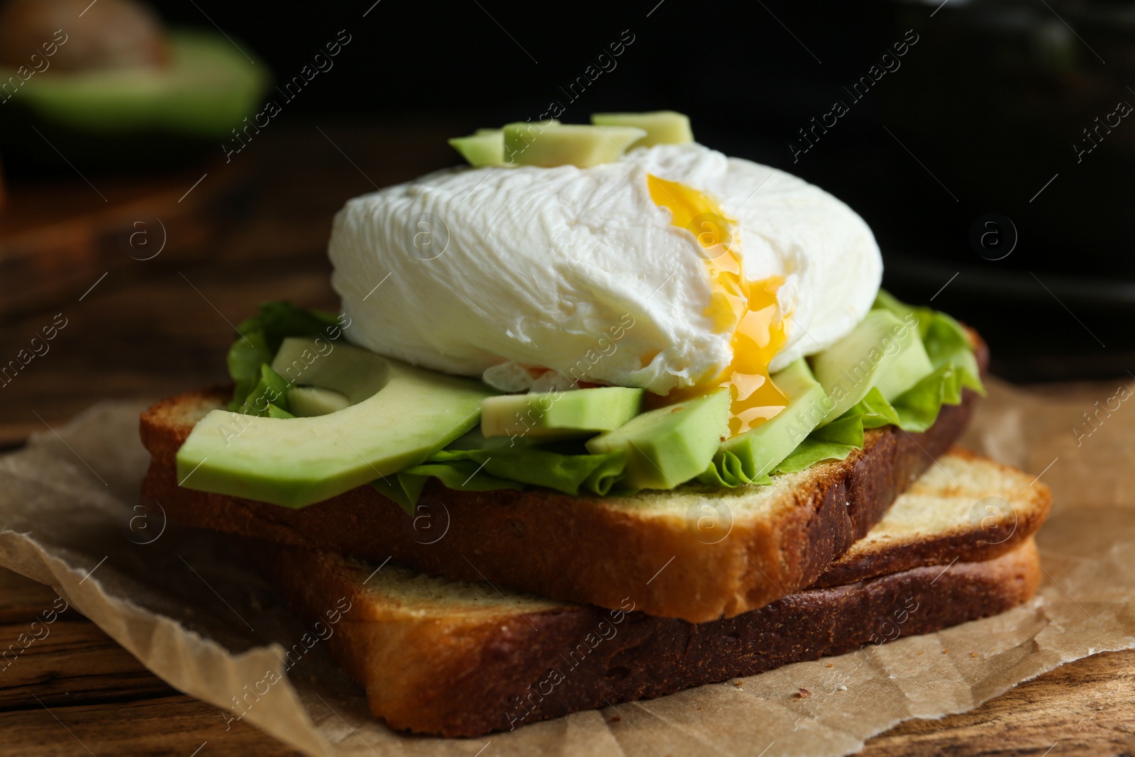 Photo of Delicious poached egg sandwich served on wooden table, closeup