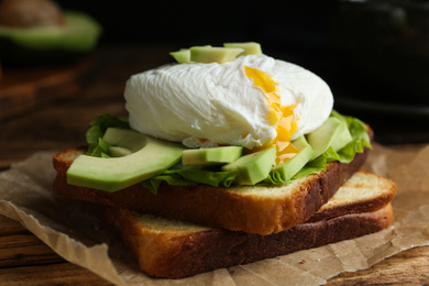 Photo of Delicious poached egg sandwich served on wooden table, closeup