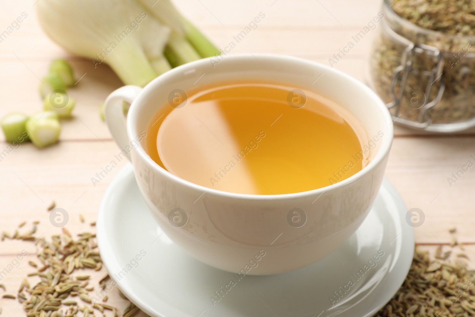 Photo of Fennel tea in cup, seeds and fresh vegetable on light wooden table, closeup