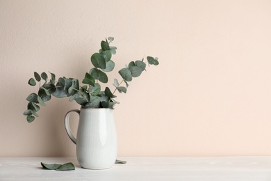 Photo of Vase with beautiful eucalyptus branches on white wooden table near beige wall. Space for text