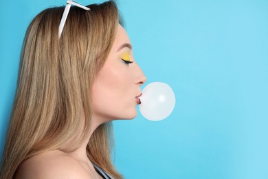 Photo of Fashionable young woman with bright makeup blowing bubblegum on light blue background, space for text