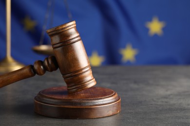 Photo of Wooden judge's gavel and Scales of justice on grey table against European Union flag, closeup. Space for text