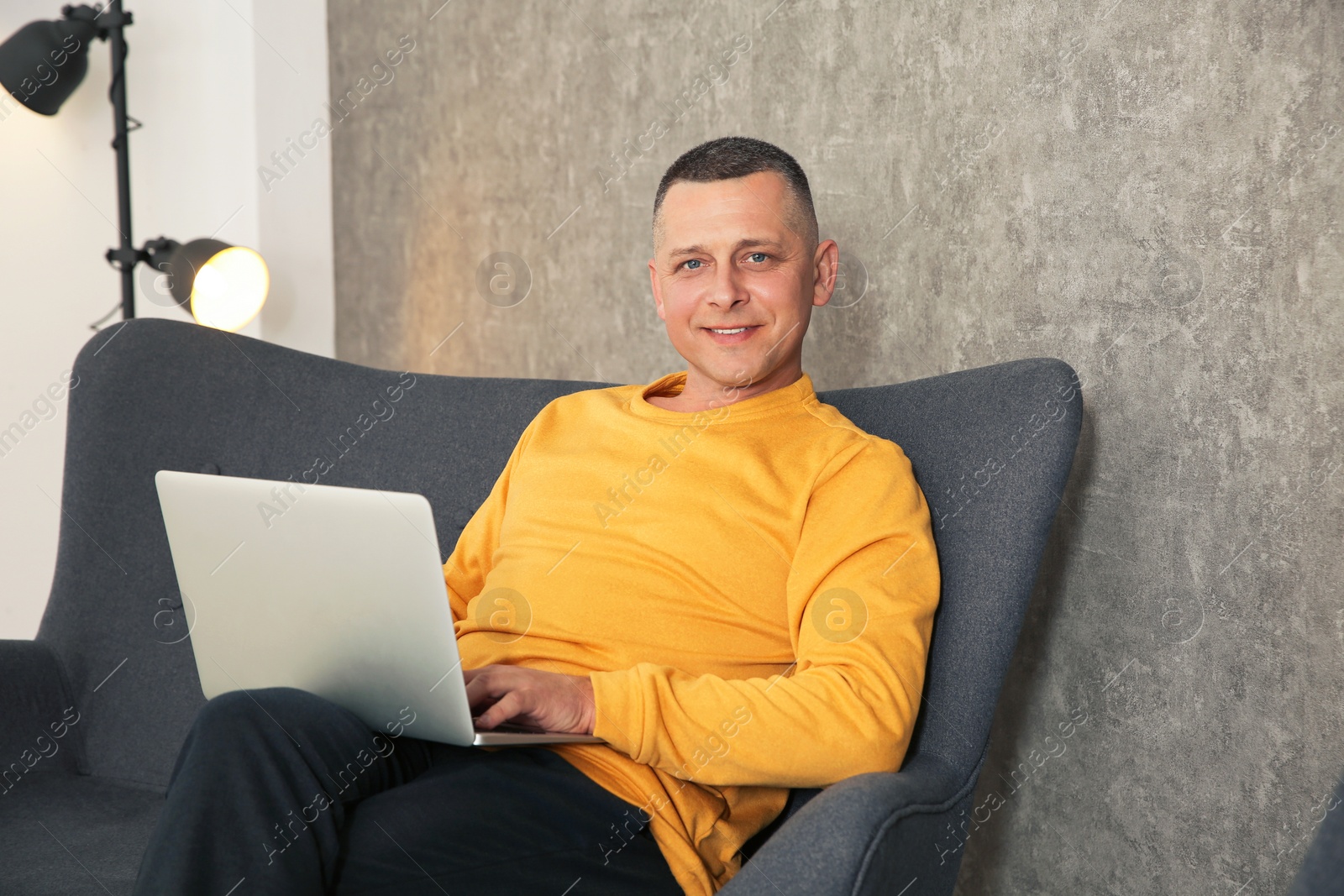 Photo of Mature man working with laptop on sofa indoors