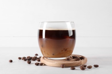 Photo of Refreshing iced coffee with milk in glass and beans on white wooden table