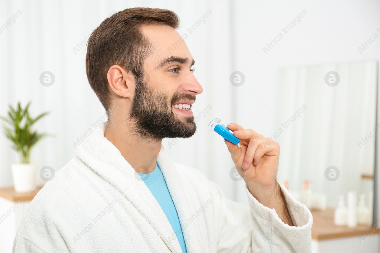 Photo of Young man using teeth whitening device at home