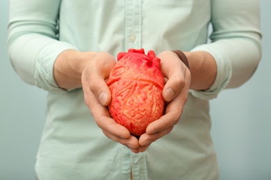 Photo of Man holding model of heart on light background, closeup. Heart attack concept
