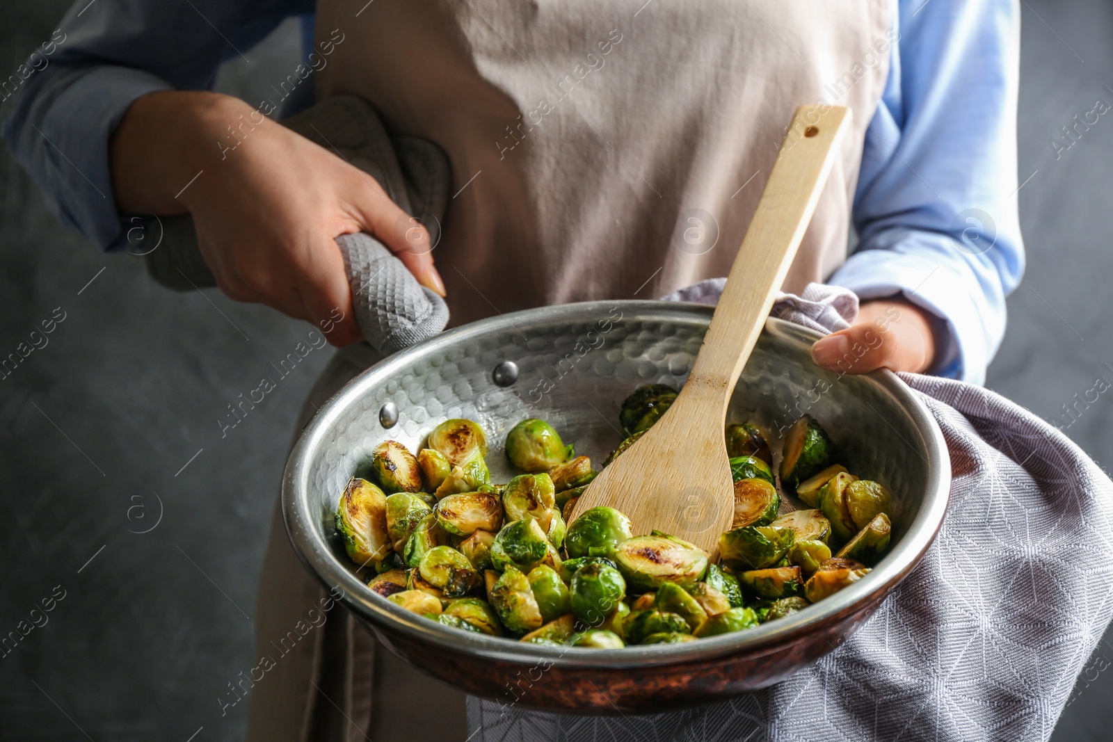 Photo of Woman with frying pan of roasted Brussels sprouts on grey background, closeup