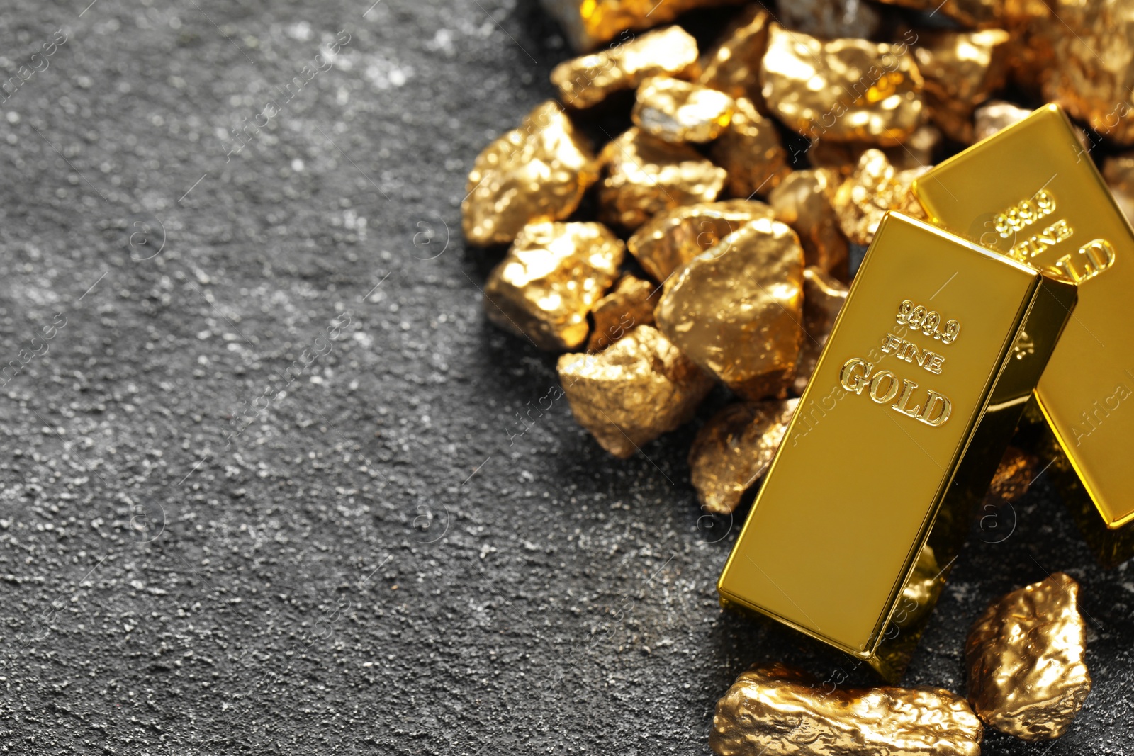 Photo of Gold ingots and nuggets on grey table. Space for text