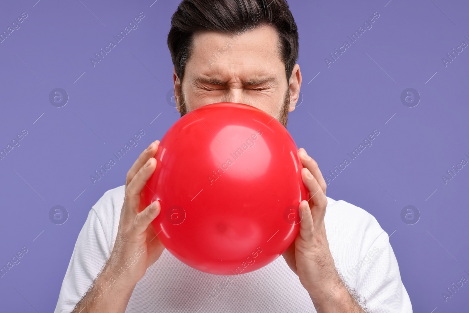 Photo of Man inflating red balloon on purple background