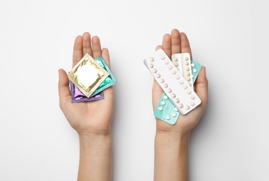 Photo of Woman holding condoms and birth control pills on white background, top view. Safe sex