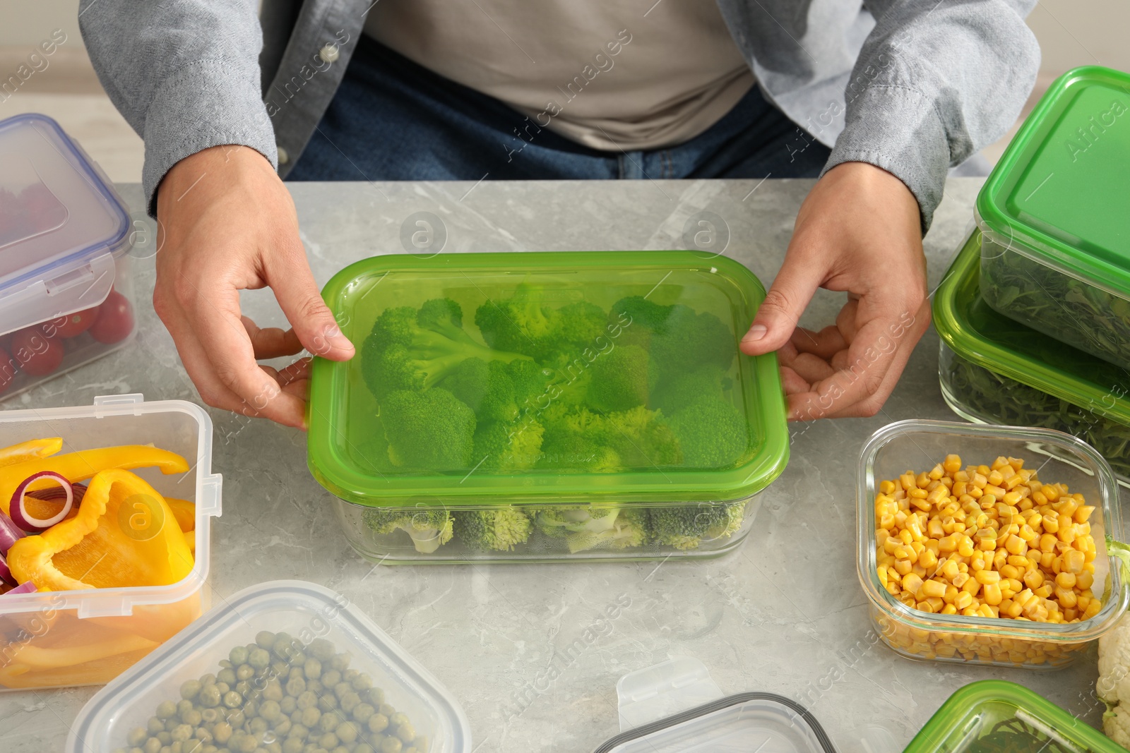 Photo of Man closing glass container with lid at light grey marble table in kitchen, closeup. Food storage