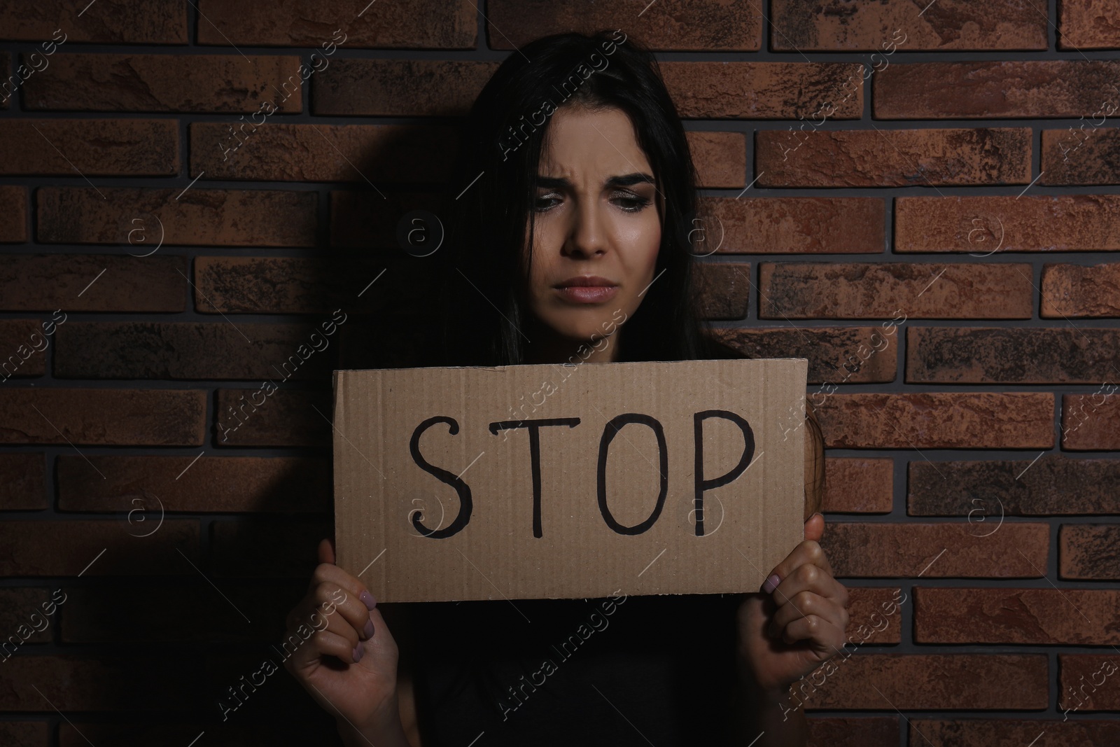 Photo of Abused young woman with sign STOP near brick wall. Domestic violence concept